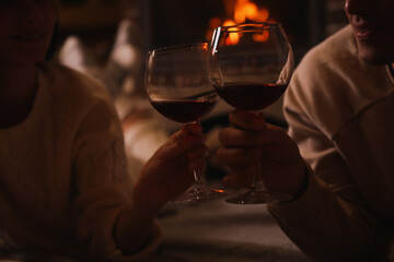 Couple with glasses of red wine near burning fireplace, closeup