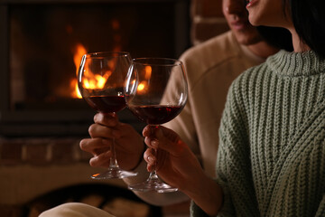 Lovely couple with glasses of wine near fireplace indoors, closeup. Winter vacation