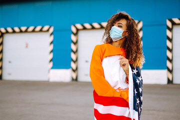 African American woman outdoors, wearing a protective mask against coronavirus and holding a USA flag.