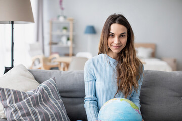 Young smiling girl holding a globe while sitting on the sofa at home.