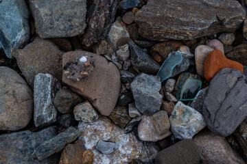 large and small rough broken colorful texture stones with glass on shore of lake, sea