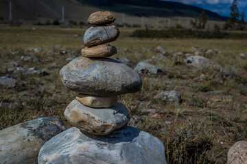 Fototapeta na wymiar Folded pyramid of different stones in steppe among the mountains