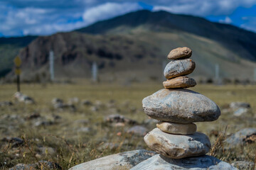 Pyramid of colorful stones against the backdrop of baikal mountains in sunlight, blue sky, clouds