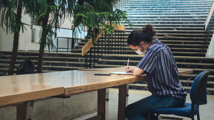  long haired and masked young university student studying alone in the library