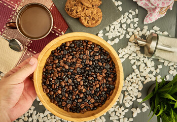 Wooden bowl with mixture of natural and roasted coffee on wooden table with cookies, sugar, and cup of coffee in overhead view