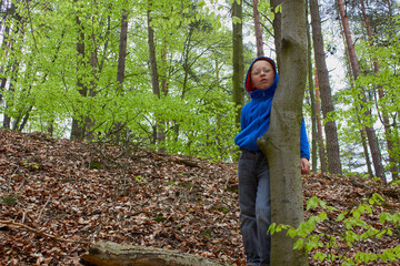 the boy hides behind a tree in autumn,Portrait of a child boy peeking from behind a tree in a forest.