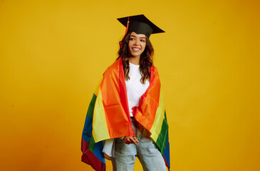 Portrait of African American  woman in a graduation hat  posing with LGBT rainbow flag. Study, education, university, college, graduate concept on yellow banner.