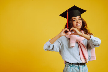 Portrait of Graduate woman in a graduation hat makes a heart with his hands. Study, education,...