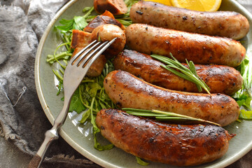 Grilled sausages with lemon and ketchup. Bavarian sausages with herbs and rosemary. Gray dark background. Gray plate and linen napkin. Closeup