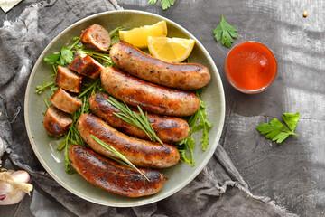 Grilled sausages with lemon and ketchup. Bavarian sausages with herbs and rosemary. Gray dark background. Gray plate and linen napkin. Free space for text