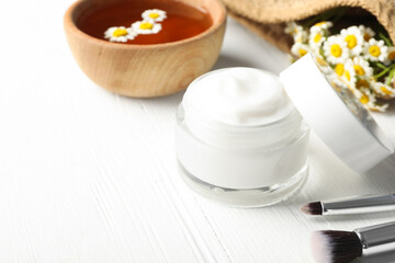 Fototapeta na wymiar Jar of cream, brushes and chamomiles on white wooden table