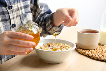 Woman putting honey into bowl with muesli at wooden table, closeup
