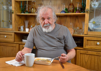 Depressold man, self isolating due to COVID-19, eating a TV dinner alone.  .Lonely old man eating by himself.