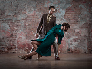 Fototapeta na wymiar a young couple - a man in a suit and a woman in a dark-turquoise dress - dancing against an old brick wall