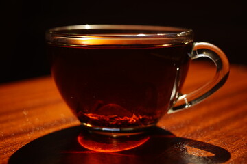 Glass cup with black tea on the brown wooden table. Closeup, side view in sunny day.