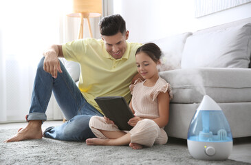 Father and daughter with tablet near modern air humidifier at home