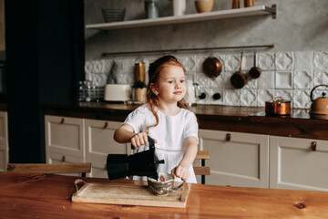 Little red-haired girl cooks in the kitchen at home, coffee