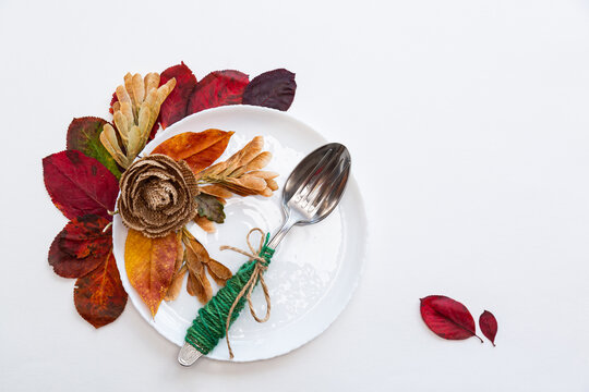 White plate and cutlery in autumn leaves on a white background. Festive autumn concept. - Powered by Adobe