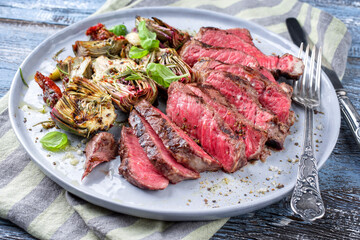 Traditional barbecue angus entrecote beef steak with artichoke hearts and herbs offered as close-up on a Modern Nordic design plate