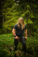 long hair Brutal man with axes in a forest
