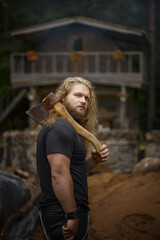 long hair Brutal man with axes near forest house