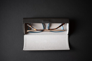 Black eyeglass case and women's eyeglasses on a black background.