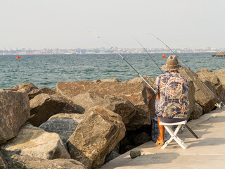 Fisherman catches fish on the embankment of the Black Sea. Panoramic seascape. Embankment of the Black Sea and the city buildings of Odessa on the horizon.