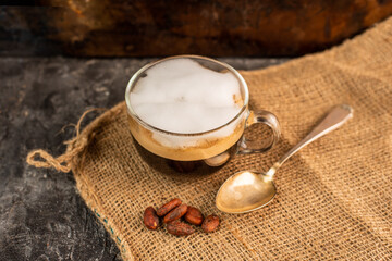 a glass of aromatic, fresh coffee with white, milk foam, on a rustic, warm background