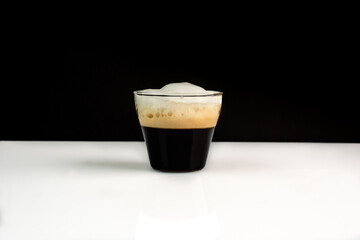 a glass of aromatic, fresh coffee with white, milk froth, on a simple black and white background