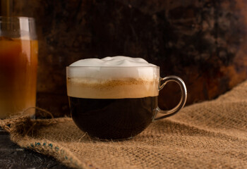 a glass of aromatic, fresh coffee with white, milk foam, on a rustic, warm background