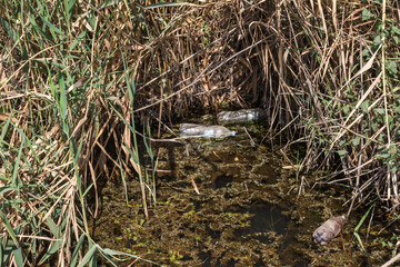 Spilled garbage to small river. Empty used dirty plastic bottles float in canal water. Pollution of environment by household waste. Ecological problem. River contaminated with various garbage