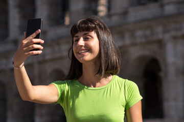 Young woman taking selfies with her smartphone in front of the Colosseum in Rome, Italy