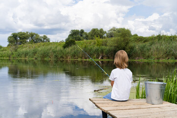 Boy fishing on a wooden bridge near a beautiful pond, beautiful nature