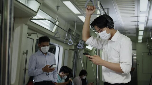 Asian business man wear face mask and read online news about invest in smartphone. Travel on modern subway transport. Wearing a mask is a modern lifestyle. Concept New Normal