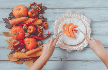 Autumn table setting, menu concept, hands with vintage fork, knife, sliced pumpkin. Thanksgiving healthy fresh food, top view, flat lay, copy space. Fallen leaves, fruits, vegetables, wooden table.