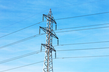 High voltage lines and power pylons in a flat and green agricultural landscape on a sunny day with cirrus clouds in the blue sky. Pylon and transmission power line