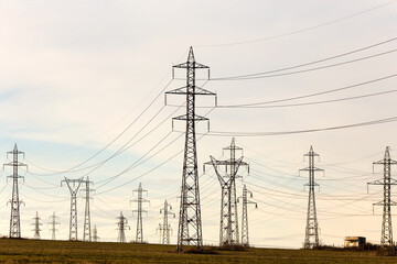 High voltage lines and power pylons in a flat and green agricultural landscape on a sunny day with cirrus clouds in the blue sky. Pylon and transmission power line