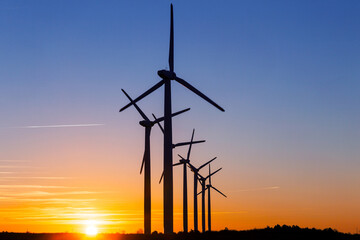 Fototapeta premium Wind Turbines at Dusk. Landscape sunset with windmills. Renewal source of electricity. Wind turbines field new technology for clean energy on mountain, sunset view with colorful twilight on sky