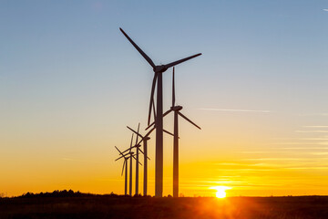 Fototapeta premium Wind Turbines at Dusk. Landscape sunset with windmills. Renewal source of electricity. Wind turbines field new technology for clean energy on mountain, sunset view with colorful twilight on sky