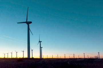 Obraz premium Wind Turbines at Dusk. Landscape sunset with windmills. Renewal source of electricity. Wind turbines field new technology for clean energy on mountain, sunset view with colorful twilight on sky