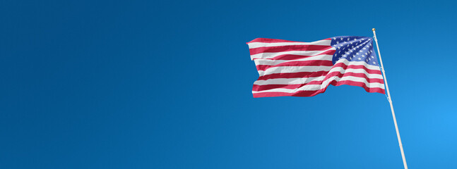 The beautiful flag of the United States of America waving against a blue sky. US national flag on background