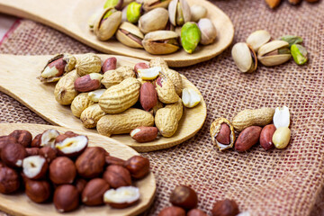 Different nuts: almonds, pistachios, peanuts, hazelnuts in light wooden spoons on beige textured textile background.