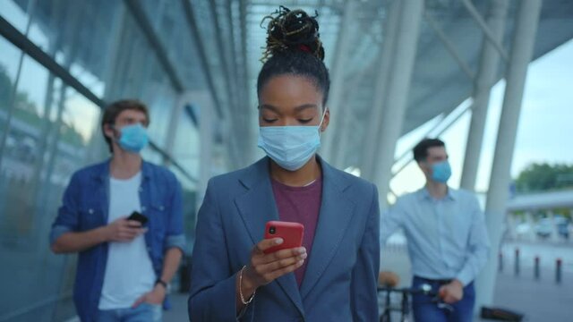 African american elegant nice-looking woman in business suit face mask holding cellphone chatting messages communicating while walking near airport terminal building.