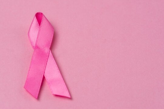 Pink ribbon breast cancer awareness symbol on pink background. Horizontal image with copy space.