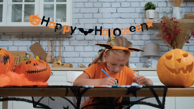 Cute Little Girl Drawing Scary Picture while Sitting at the Table in Halloween. Holidays and Halloween Decorations Concept
