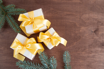 Three gift boxes tied with a gold ribbon and fir branches on a dark wooden background. New Year card, top view. Copy space for text.