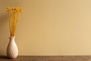 Vase of yellow dry flowers on wooden table with brown background. copy space