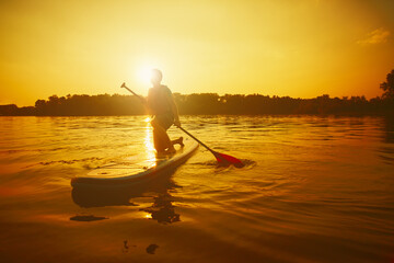 Silhouette of man paddling on paddle board at sunset. Water sport near the beach on sunset