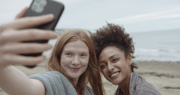 Female friends together on beach taking selfie with smart phone outdoors on beach