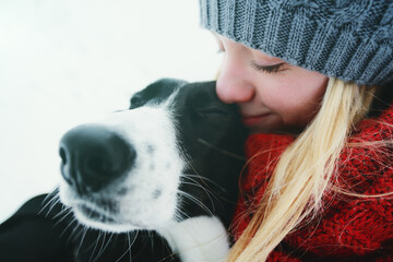Young Caucasian woman playing with her dog in the snow in winter in the forest.